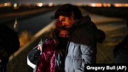 El migrante cubano Mario Pérez sostiene a su esposa mientras esperan ser procesados para solicitar asilo, luego de cruzar la frontera hacia EEUU, el 6 de enero de 2023, cerca de Yuma, Arizona. (AP/Gregory Bull)