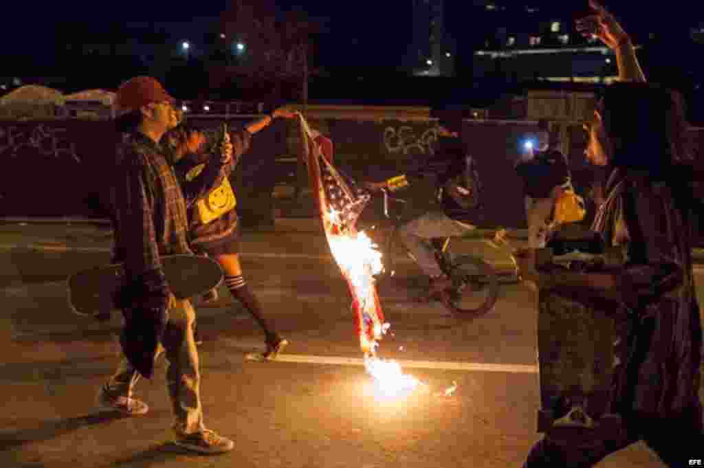 Un manifestante lleva una bandera estadounidense en llamas durante una protesta en Oakland, California (EEUU) contra la elección del republicano Donald Trump como nuevo presidente estadounidense.  