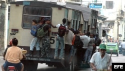 Varias personas viajan colgando de un ómnibus, popularmente conocido como camello