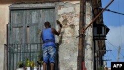 Un hombre repara la fachada de un viejo edificio en La Habana.