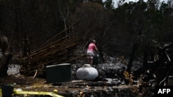 Una mujer cuelga un cartel de prohibido el paso en el sitio de una casa destruida por los incendios forestales de Maui en Kula, Hawai, el 13 de agosto de 2023.