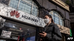 Mujer con mascarilla delando de una tienda de la empresa Huawei en China.